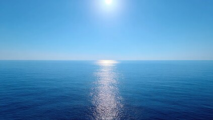 Obraz premium Calm ocean scene at midday, sun reflecting brightly on a flat, still, deep blue water surface extending to the horizon under a clear, vibrant sky