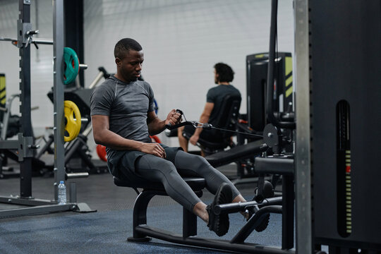 Young African American man doing workout in modern gym exercising with use of cable row machine, copy space - Powered by Adobe