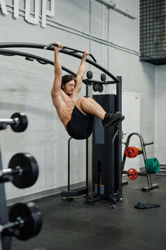 Vertical wide shot of young Caucasian man with muscular body doing pull-ups in modern gym, copy space