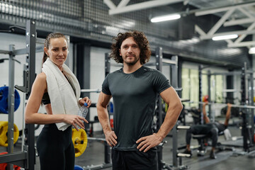 Cheerful sporty young Caucasian man and woman posing for camera in modern gym, medium portrait, copy space