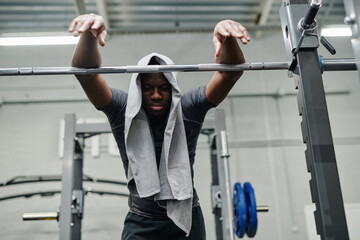 Low angle view of tired sporty young Black man with towel on head taking rest after doing exercise in gym