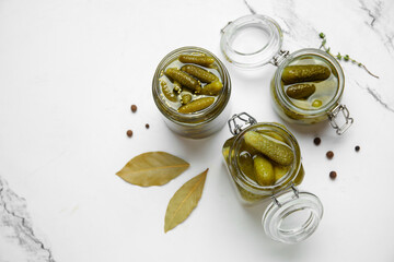 Jars with tasty pickled cucumbers, peppercorns and bay leaves on white background