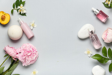 Natural cosmetic products with flowers, peach and spa stones on grey background with space for text