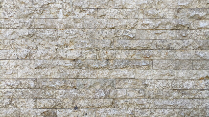 Close-up of rough beige stone brick wall texture with natural patterns and irregular surfaces, perfect for backgrounds, architectural design elements, and construction material concepts.