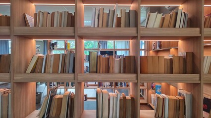 A close-up view of neatly arranged books on wooden shelves, illuminated by soft lighting, in a modern library or reading space. 