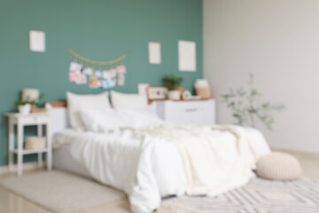 Blurred view of bedroom with big comfortable bed, bedside table and chest of drawers