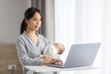 Mother caring baby while working on laptop