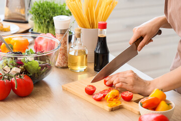 Young woman cutting fresh tomato in kitchen, closeup