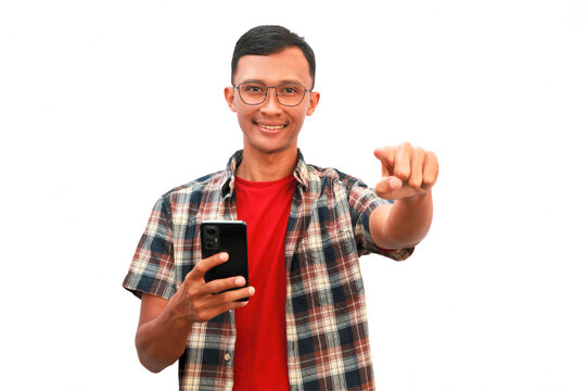 A man holding a cell phone points at the camera with a smiling expression. - Powered by Adobe