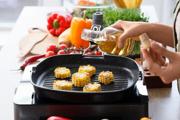 Young woman with oil frying corn on grill pan in kitchen, closeup