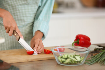 Young woman cutting tomato at table in kitchen, closeup