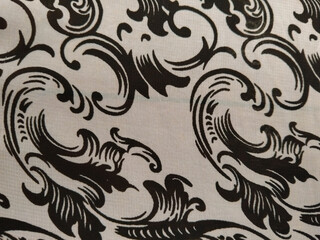 Black ornate floral patterns on a white fabric background, creating an elegant and classic decorative design.