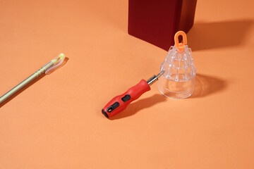 On an orange background, there is a screwdriver, a red book, and a yellow ballpoint pen