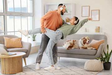 Young couple in headphones with Australian Shepherd dog dancing at home