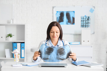 Female doctor with x-ray image of lungs at table in clinic