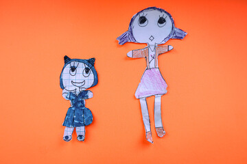 ​Two children's paper cutout dolls stand on a bright orange background. The shot conveys an atmosphere of childhood, creativity, and handcraft.