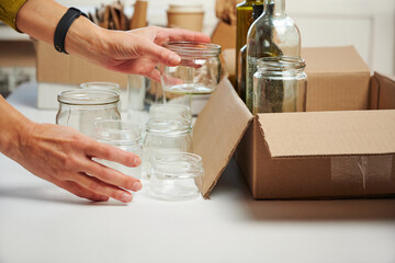 Garbage separation concept. Female hands separate glass cans into cardboard box at home. Waste segregation, waste sorting, waste recycle.