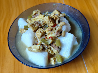 A bowl of vegetable rice cakes. Lontong vegetable in coconut milk sauce with tofu, beef which is a typical Indonesian food. Served on a wooden table.