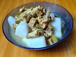 A bowl of vegetable rice cakes. Lontong vegetable in coconut milk sauce with tofu, beef which is a typical Indonesian food. Served on a wooden table.