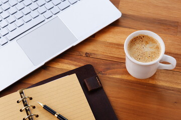 机にリング式のシステム手帳を広げ、淹れたてのコーヒー（カフェ・ラテ）を飲みながら、パソコンでデスクワークをしているイメージ
