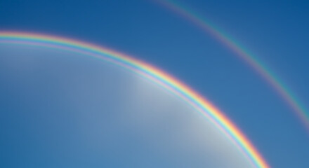 Vibrant rainbow arching across a bright blue sky with fluffy clouds — colorful nature scenery