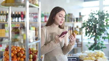  Young woman buyer scanning qr code for yellow smoothie in bottle in grocery store