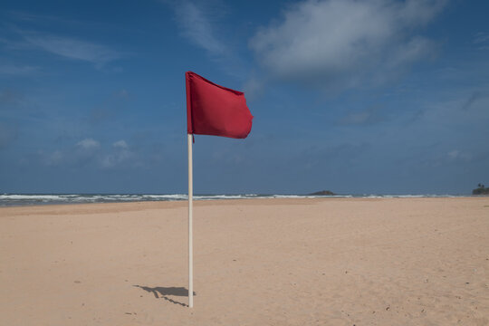 red flag on the beach with blue sky and clouds and dangerous rough sea 