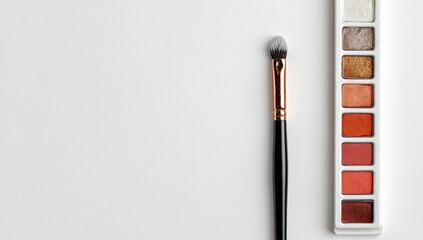 A makeup brush rests beside a palette of earthy orange eyeshadows on a white background; ample copy space