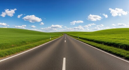 Fototapeta premium Asphalt road stretching to horizon between green fields, blue sky, fluffy clouds