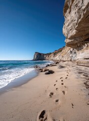 Coastal scene with footprints on sandy beach.  Cliff face and ocean waves