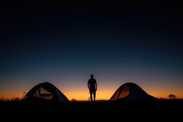 Silhouette of a solo camper at sunrise, two tents