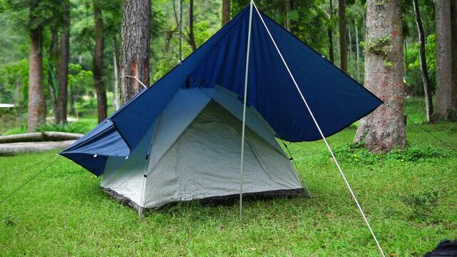 A camping tent equipped with a tarp flysheet for extra protection from the elements. Located in a beautiful camping area with a backdrop of shady trees.