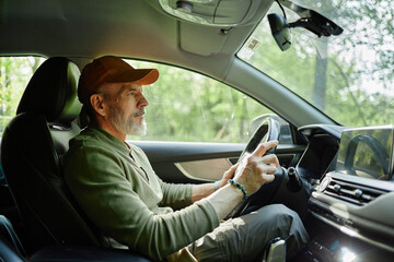 Caucasian man driving car, holding steering wheel with both hands, looking focused ahead, sitting...