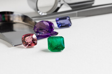 Natural coloured gem stones closeup on the white background. Emerald, Sapphire, Amethyst, Spinel, Tourmaline.