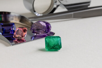 Natural coloured gem stones closeup on the white background. Emerald, Sapphire, Amethyst, Spinel, Tourmaline.