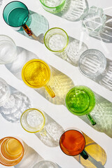 Colored Glasses pattern with shadow and sunlight reflection white background, minimal aesthetic top view summer still life, refraction at shine drink, caustic effect, green yellow glass cups