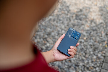 A person is holding a cell phone in their hand. The phone is black and has a cracked screen