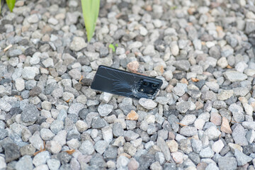 A cell phone is laying on the ground in a pile of rocks. The phone is cracked and broken