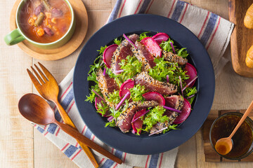 【まぐろのたたきサラダ】オリーブオイルに漬け込み下味をつけた後、胡麻をつけてグリルした鮪を紅だいこんと山葵菜で和えたサラダです。ドレッシングも山葵の効いたピリ辛風味にしました。