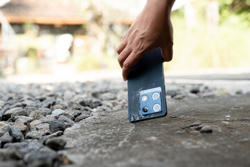 A person is holding a cell phone in their hand. The phone is black and has a square shape