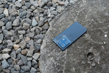 A person is holding a cell phone in their hand. The phone is black and has a cracked screen