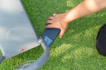 A person is holding a cell phone in their hand. The phone is laying on the grass. The grass is green and the person is standing on it