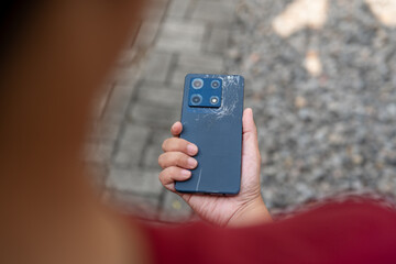 A person is holding a cell phone with a cracked screen. The phone is black and has a large screen