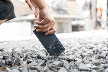 A person is holding a cell phone in their hand. The phone is black and has a cracked screen