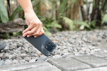 A person is holding a cell phone in their hand. The phone is black and has a cracked screen