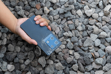 A person is holding a cell phone in their hand. The phone is black and has a cracked screen