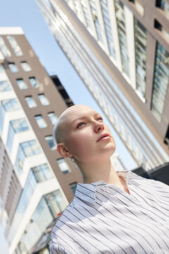 Vertical medium closeup dutch angle of young Caucasian woman with alopecia standing outdoors at business district