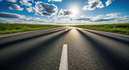 Fototapeta premium Paved road stretches to horizon under bright sun and cumulus clouds