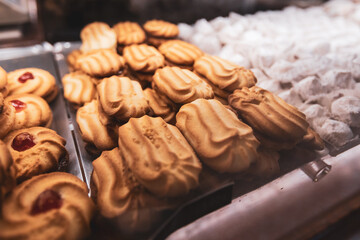 A close-up shot of freshly baked shortbread cookies with a distinct grooved pattern and whipped cream frosting, displayed on a tray in a bakery.
