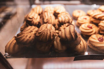 A close-up shot of freshly baked shortbread cookies with a distinct grooved pattern and whipped cream frosting, displayed on a tray in a bakery.
